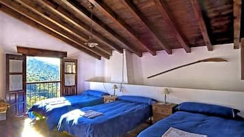 Une chambre avec deux lits, des poutres en bois au plafond, une fenêtre donnant sur une montagne et une petite table avec une lampe.