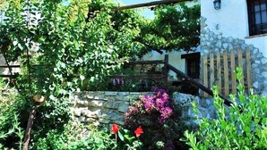 Eine rustikale Steinmauer mit einer Holztreppe, die zu einem Balkon führt, umgeben von üppigem Grün und blühenden Pflanzen.