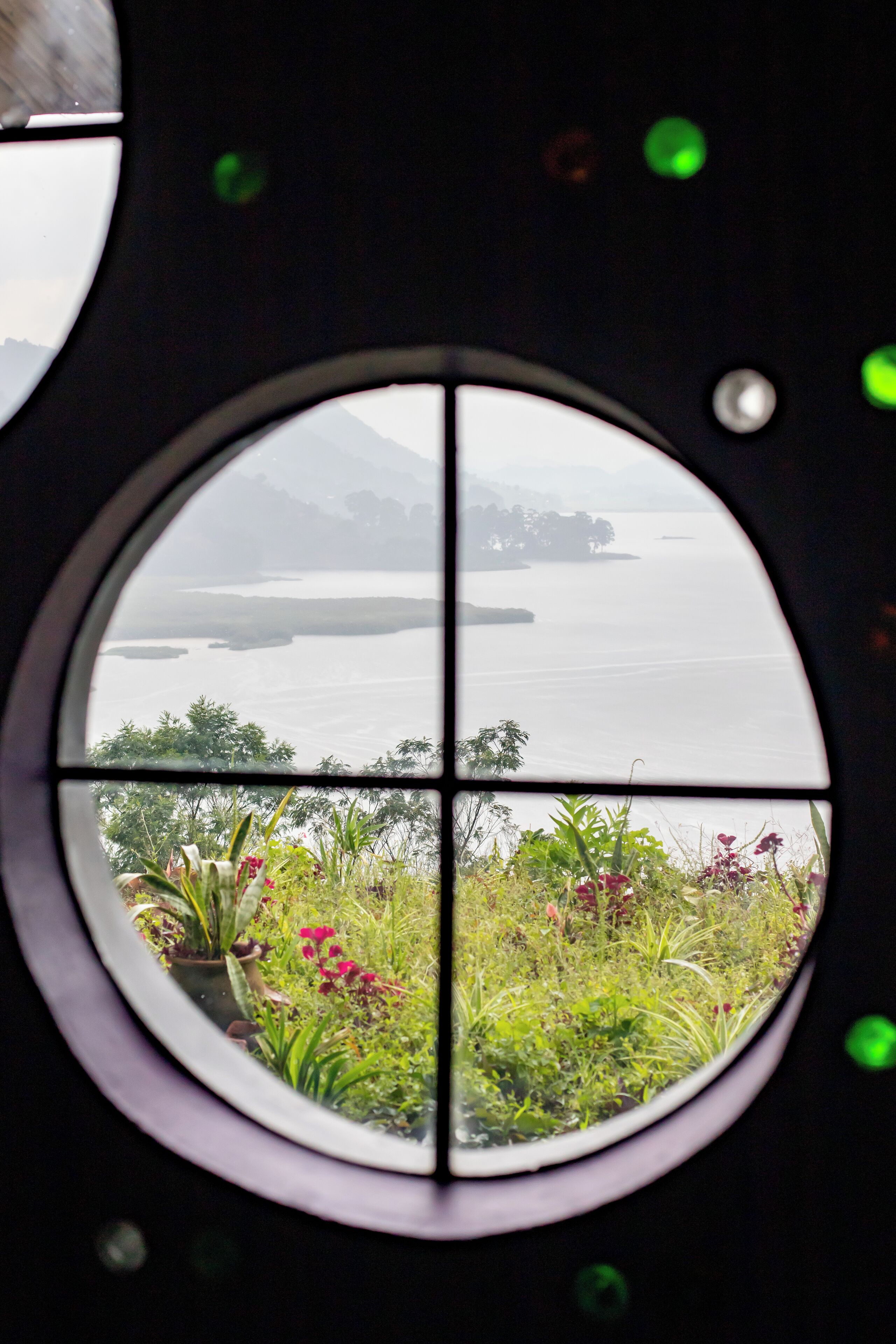 A circular window with a view of a body of water and greenery.