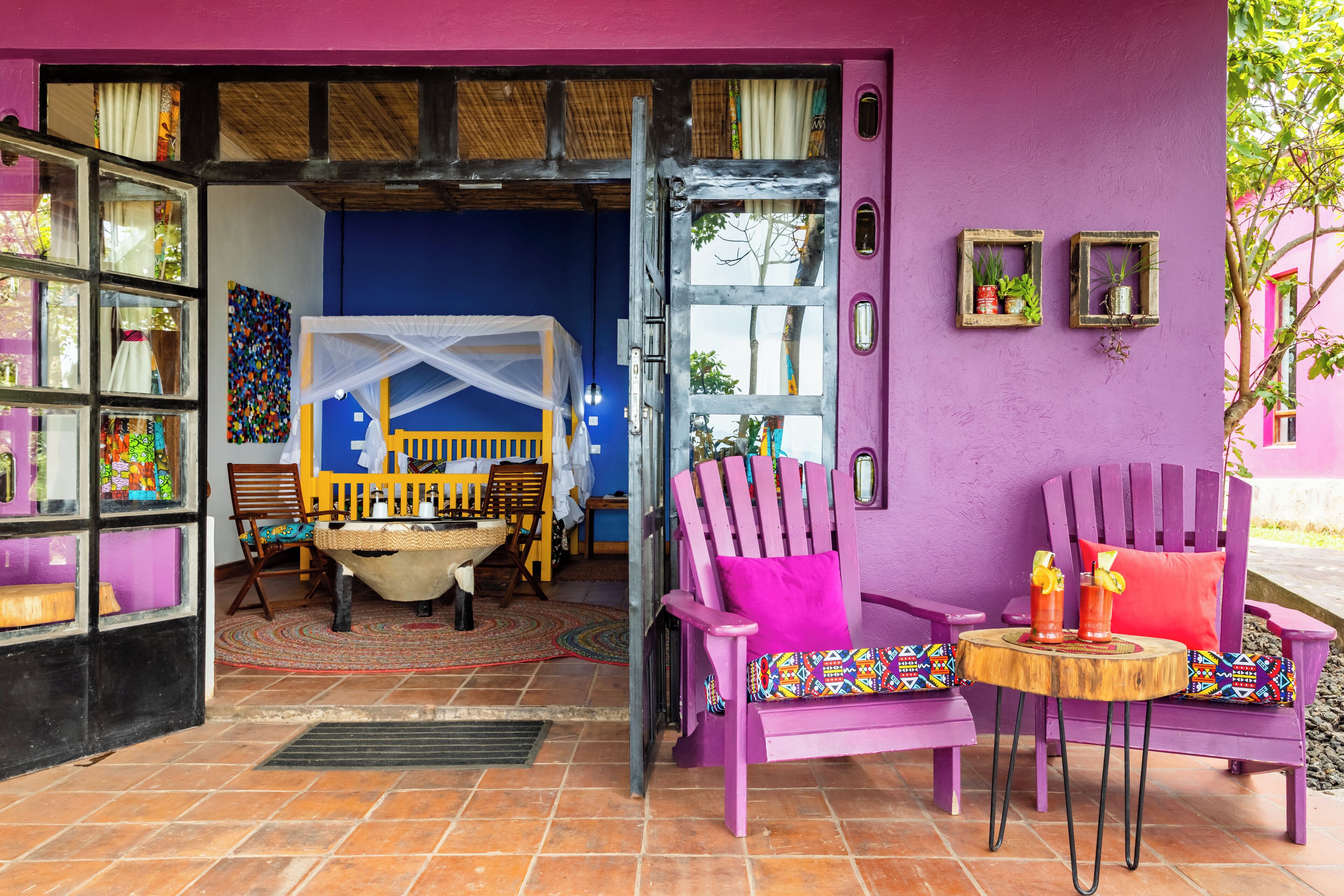 A vibrant room with a purple wall, a wooden chair, a small table, and a bed with a canopy.
