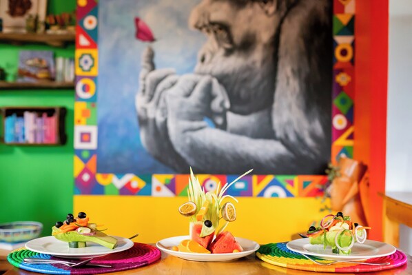 Um interior colorido com uma grande pintura abstrata, uma mesa com três pratos de comida e um design vibrante na parede.