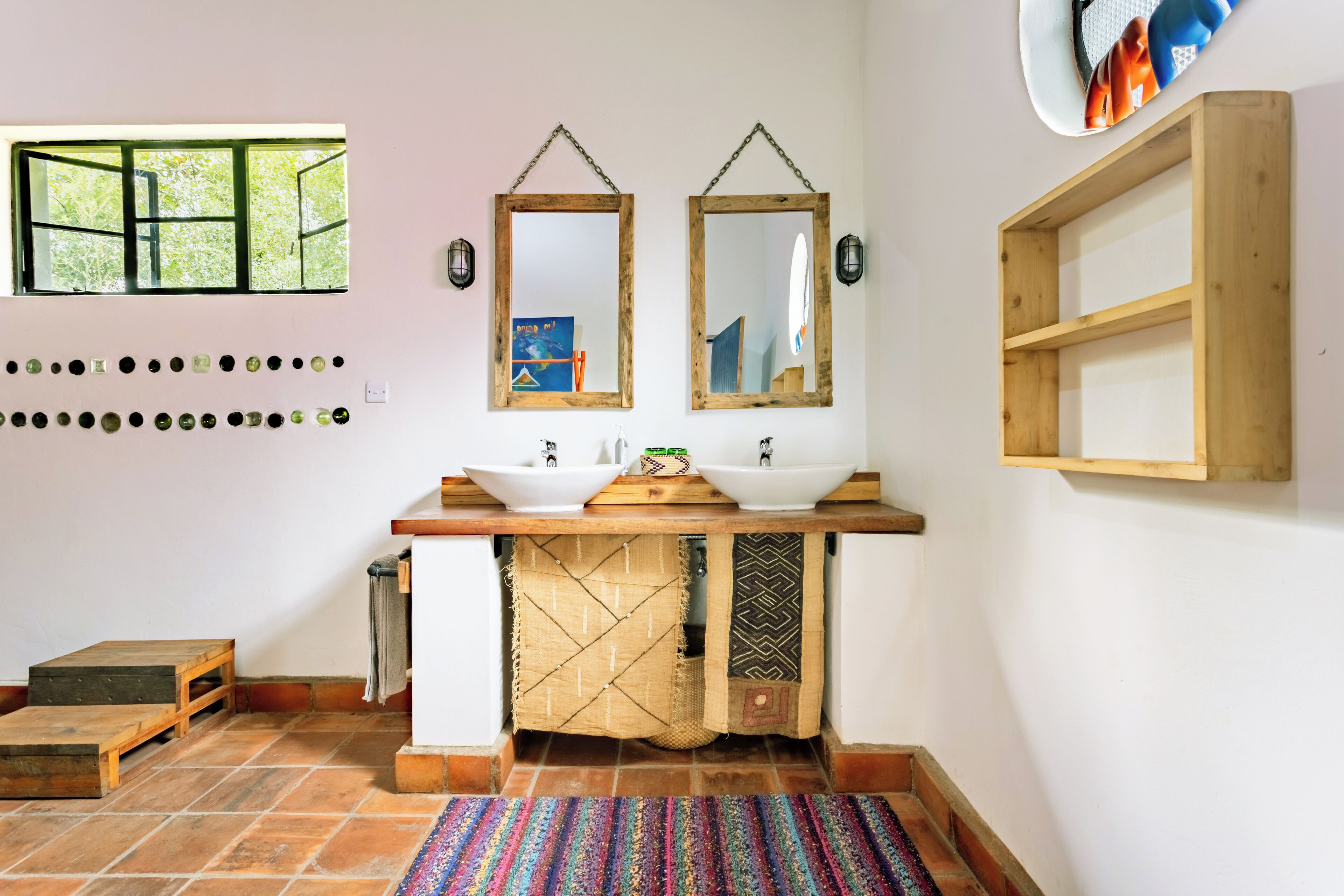 Un baño con dos lavamanos, estantes de madera, una ventana y suelo de baldosas.