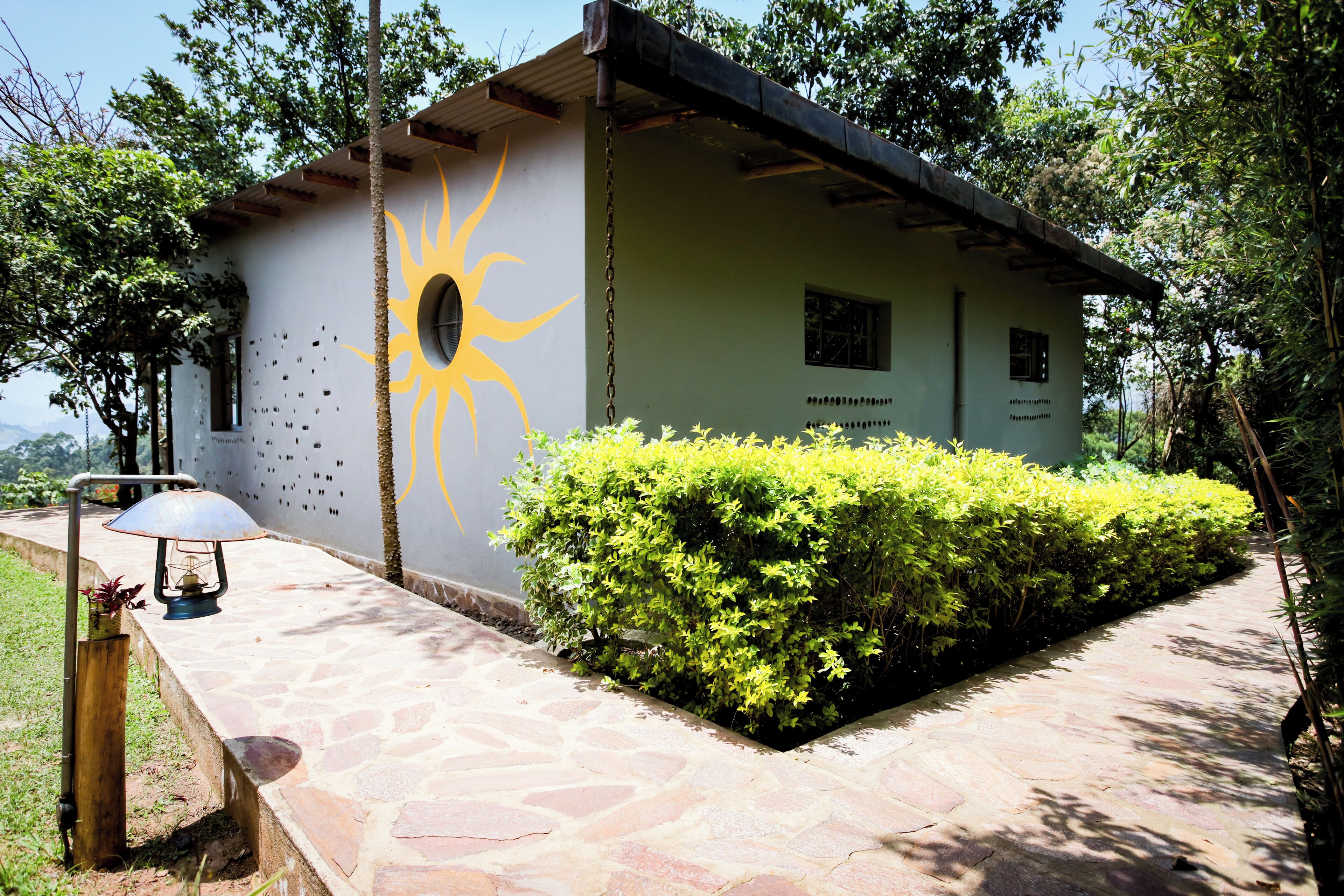 A small building with a sun mural, surrounded by greenery and a stone pathway.
