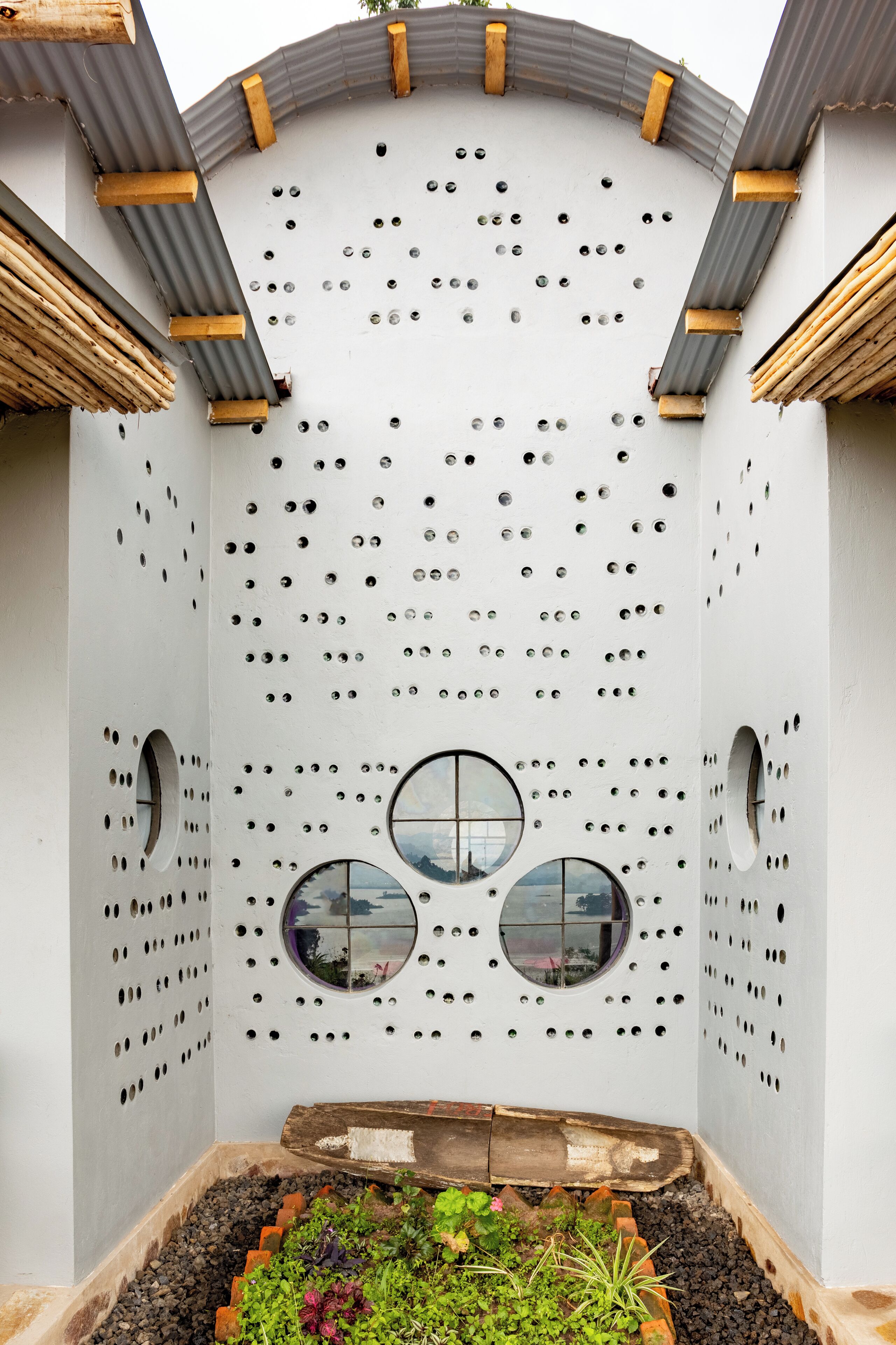 A modern building with a unique perforated wall design, circular windows, and a garden area at the base.