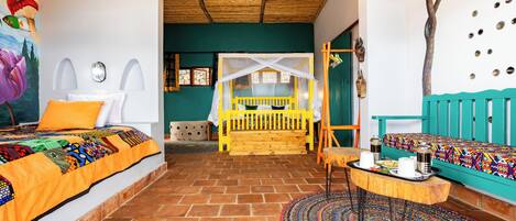 Una habitación con una cama, un banco, una mesa con tazas y una alfombra colorida.