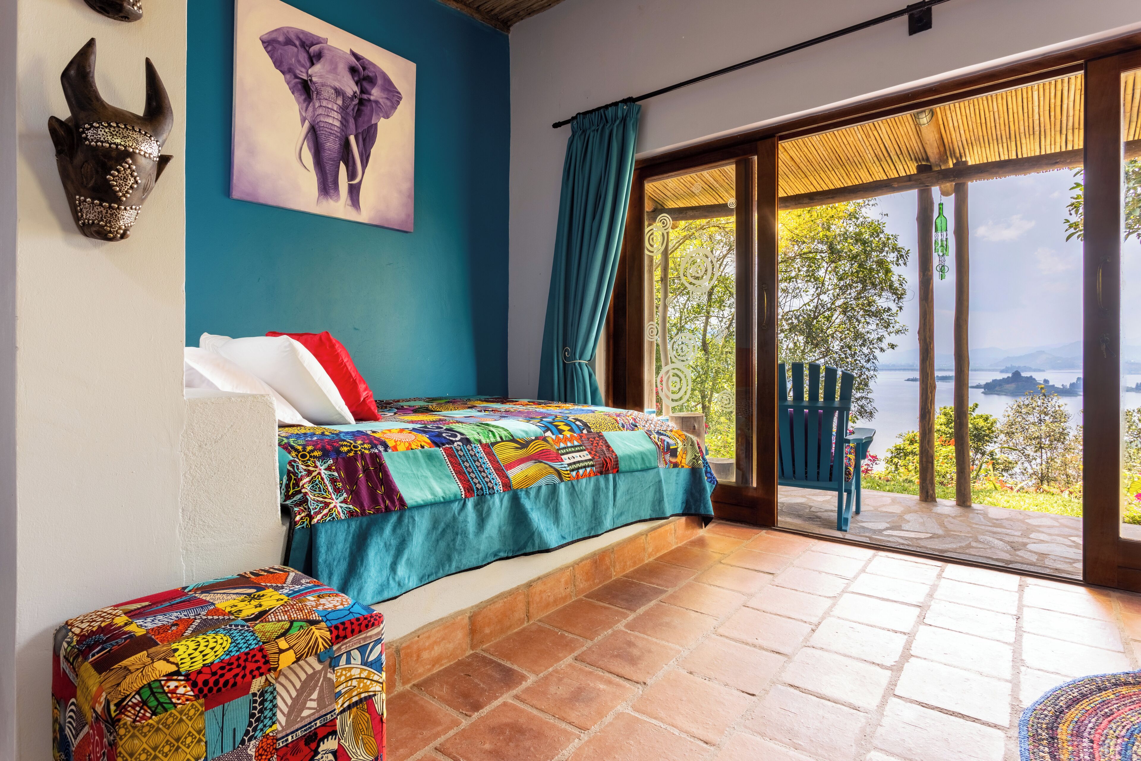 A bedroom with a large bed, a colorful quilt, a chair, and a view of the outdoors.