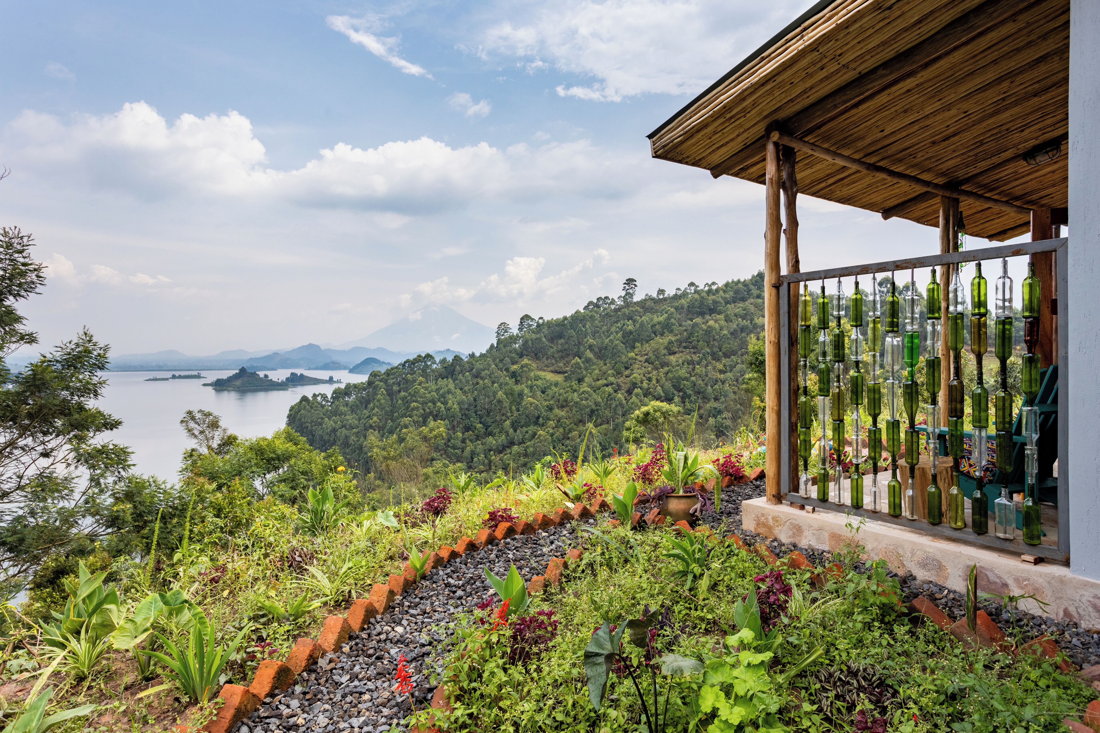 Ein Garten mit vielfältigen Pflanzen und einer hölzernen Pergola mit Blick auf einen See und Berge.