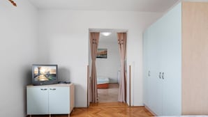 Un dormitorio con cama, televisión en un mueble, armario y puerta que da a otra habitación.