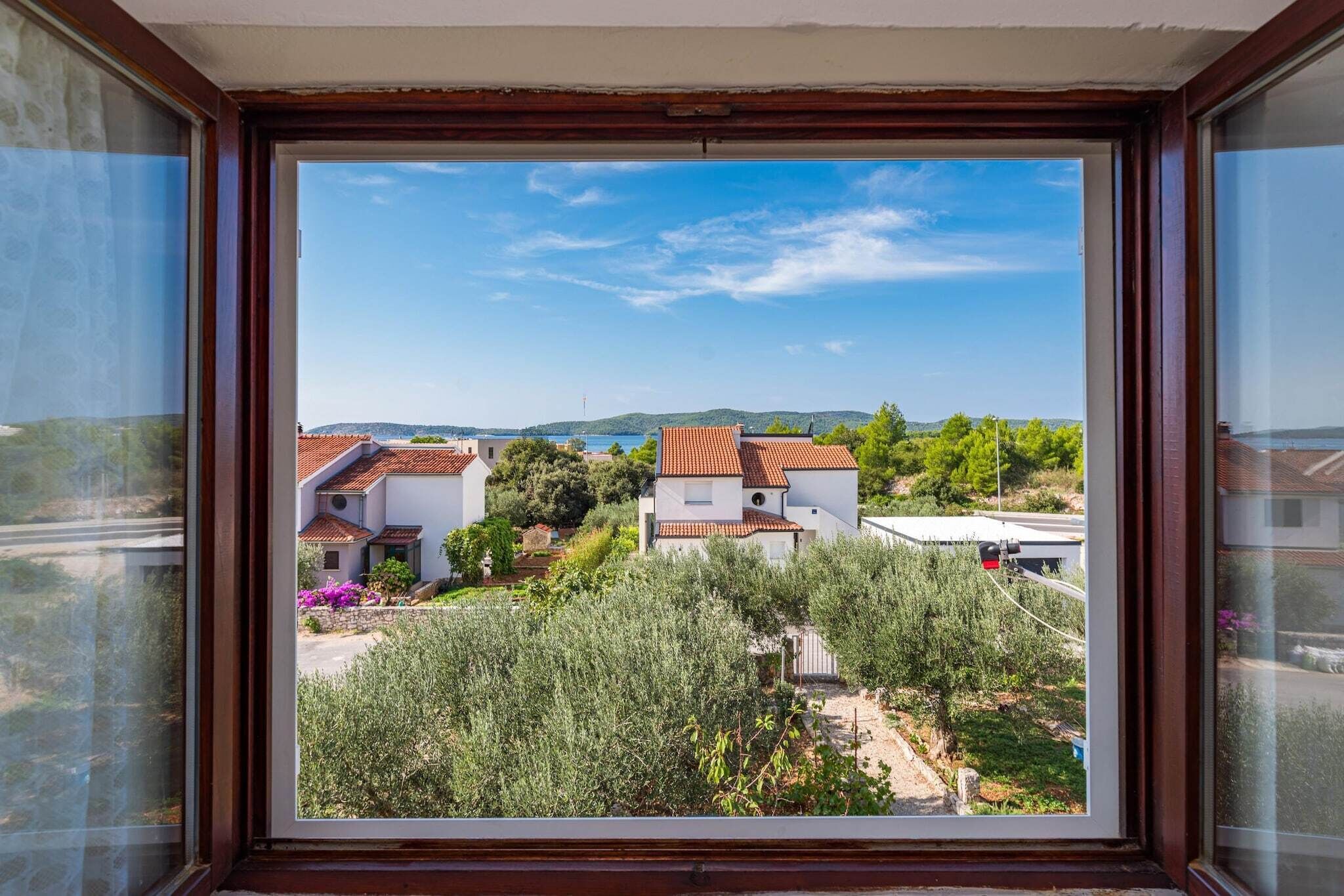 Vista desde una ventana con vista a una zona residencial con casas, vegetación y cielo despejado.