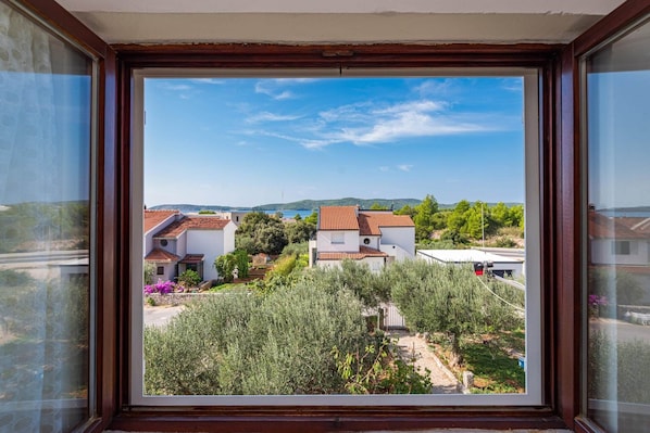 A view from a window overlooking a residential area with houses, greenery, and a clear sky.