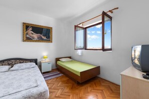 Una camera da letto con un letto matrimoniale, un letto singolo, un comodino, una lampada, un televisore e una finestra.