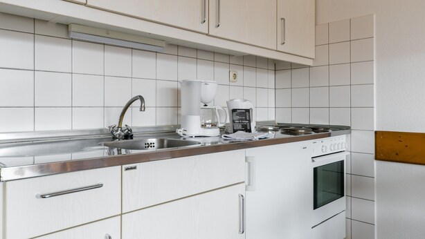 A modern kitchen with white cabinetry, a stainless steel sink, a coffee maker, and an oven. - Appartement im Panoramic Hotel Bad Lauterberg (Bad Lauterberg)