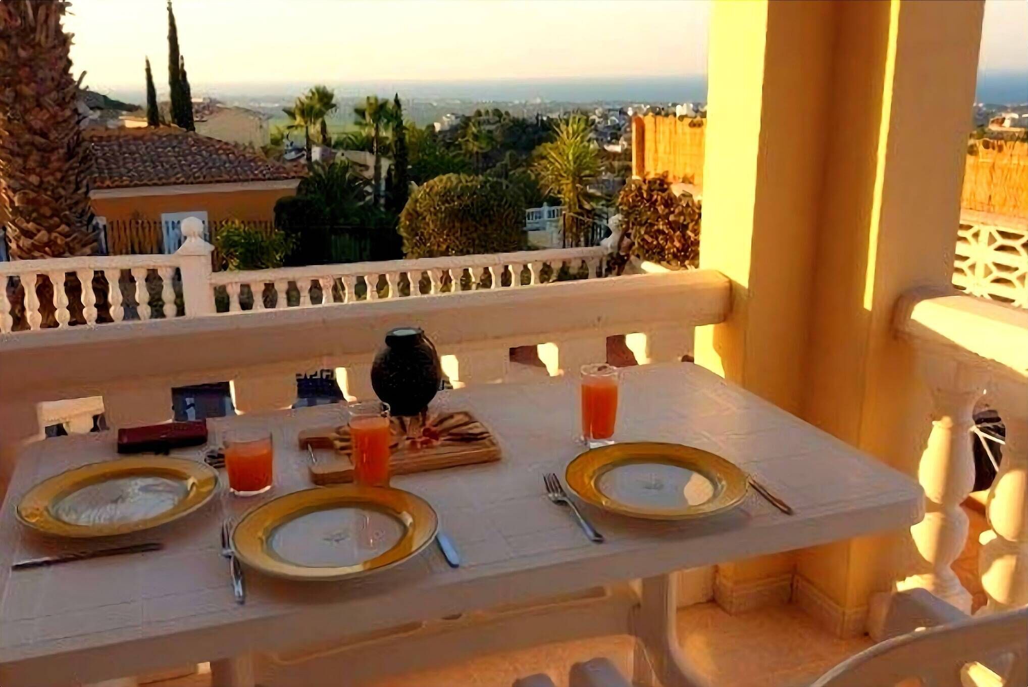 Une table de balcon, dressée avec des assiettes, des couverts et des boissons, d’où l’on peut admirer un paysage urbain avec des palmiers et des immeubles.