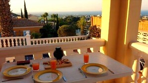 A balcony table set with plates, cutlery, and drinks, overlooking a cityscape with palm trees and buildings.