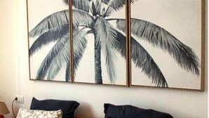 A room with a bed, two pillows, and a large wall art of a palm tree.