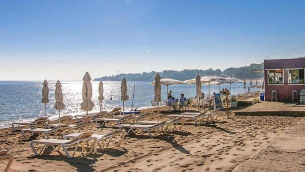 A beach with sun loungers and umbrellas, a building with a restaurant, and the sea in the background.