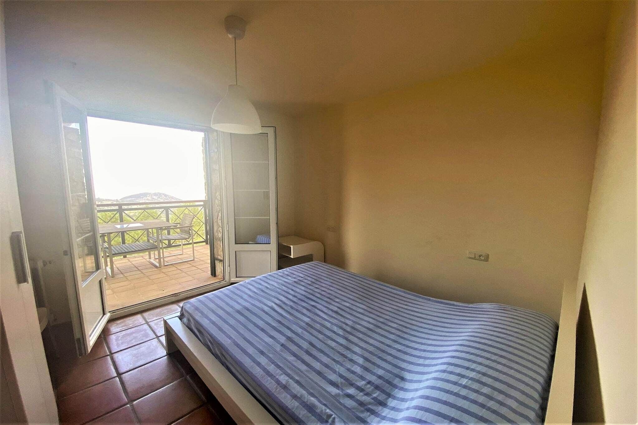 Een slaapkamer met een bed, een nachtkastje, een stoel, een raam en een balkon.