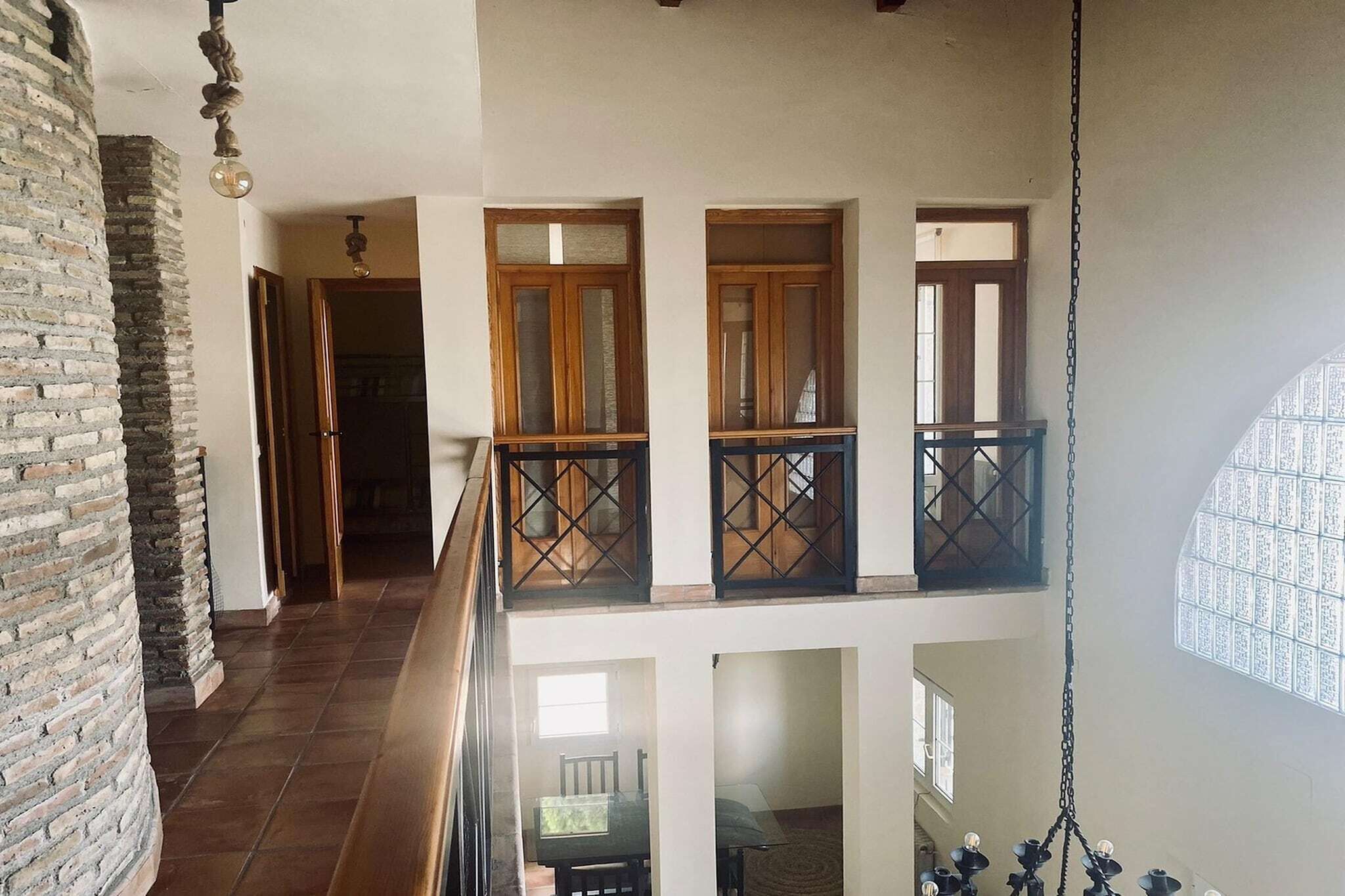 A multi-level interior with a brick wall, wooden doors, and a balcony with a metal railing.