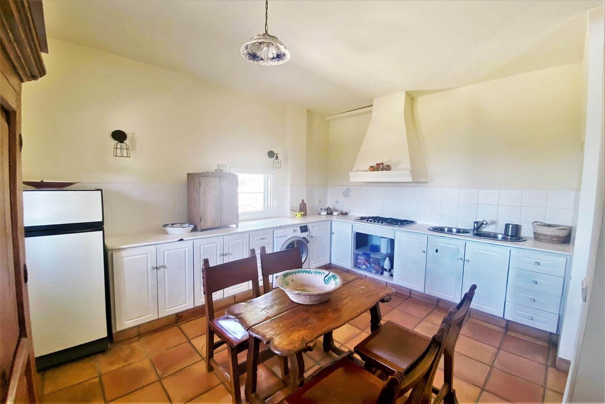 A compact kitchen with white cabinets, a wooden dining table, and a hanging light fixture.