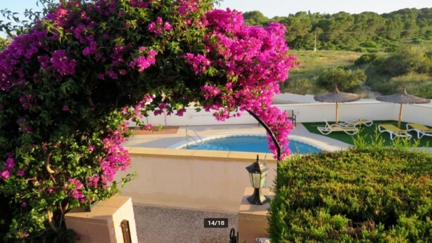 Een zwembadgedeelte met een pergola bedekt met roze bloemen, een loungehoek bij het zwembad en uitzicht op het omliggende landschap.