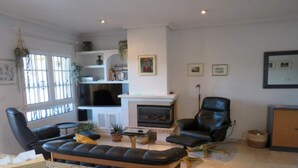 Een woonkamer met een open haard, zwarte leren fauteuils, een bank en een boekenkast.