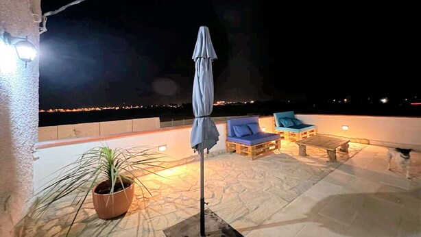 A rooftop terrace with a potted plant, a covered umbrella, and two blue lounge chairs.