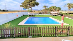 A swimming pool with a wooden fence, surrounded by greenery and a clear sky.