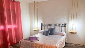 A bedroom with a bed, red curtains, and a hanging light fixture.