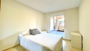 Une chambre avec un lit, une table de chevet et un petit meuble. Une porte-fenêtre coulissante donne accès à un espace extérieur.