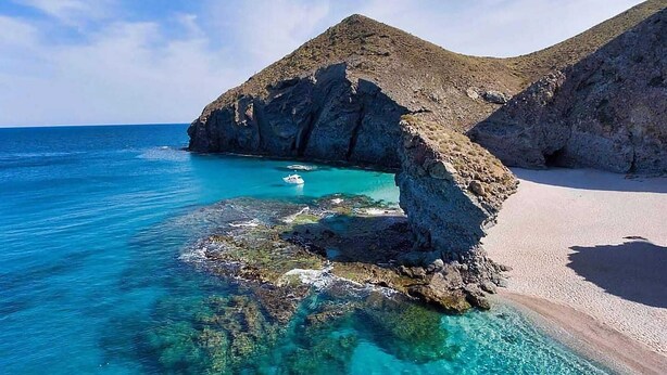 Un paysage côtier caractérisé par des eaux turquoise limpides, des formations rocheuses et une plage de sable.