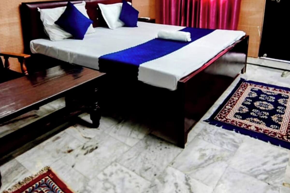 A hotel room with a bed, a wooden bench, a patterned wall, a red curtain, and a marble floor.