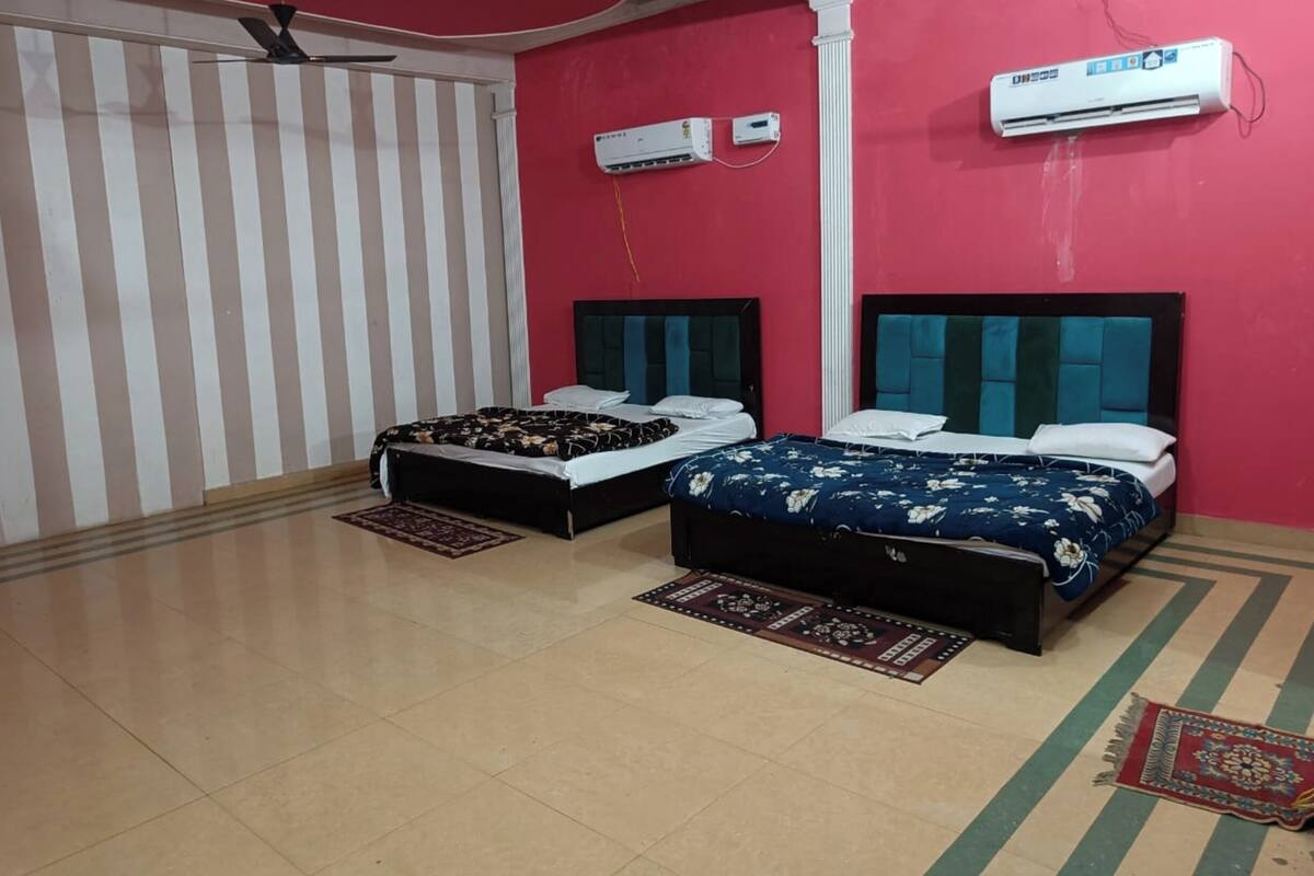 A room with two beds, a ceiling fan, and two wall-mounted air conditioners.