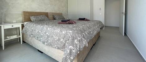 A bedroom with a large bed, a nightstand, a wardrobe, and a door leading to another room.