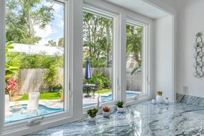 A spacious room with large windows, a marble countertop, and a view of a backyard with a pool and patio furniture.