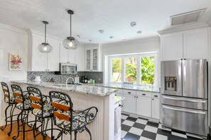 Een moderne keuken met witte kasten, een roestvrijstalen koelkast, een marmeren aanrecht en een geruite vloer.