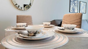 A dining table set with floral-patterned bowls and plates, surrounded by cushioned chairs.