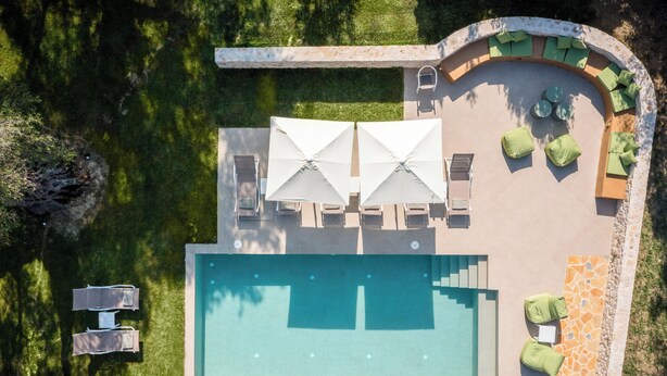 An aerial view of a swimming pool area with two umbrellas, lounge chairs, and a seating area with cushions.