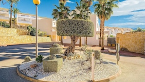 A landscaped area with a neatly trimmed tree, a street lamp, and a stone wall. - Bungalow Orihuela Costa Sunset and Pool (Relleu)