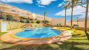 A swimming pool with a surrounding stone wall, palm trees, and a clear blue sky. - Bungalow Orihuela Costa Sunset and Pool (Relleu)