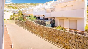 A row of white buildings with balconies, a stone retaining wall, and a clear blue sky. - Bungalow Orihuela Costa Sunset and Pool (Relleu)