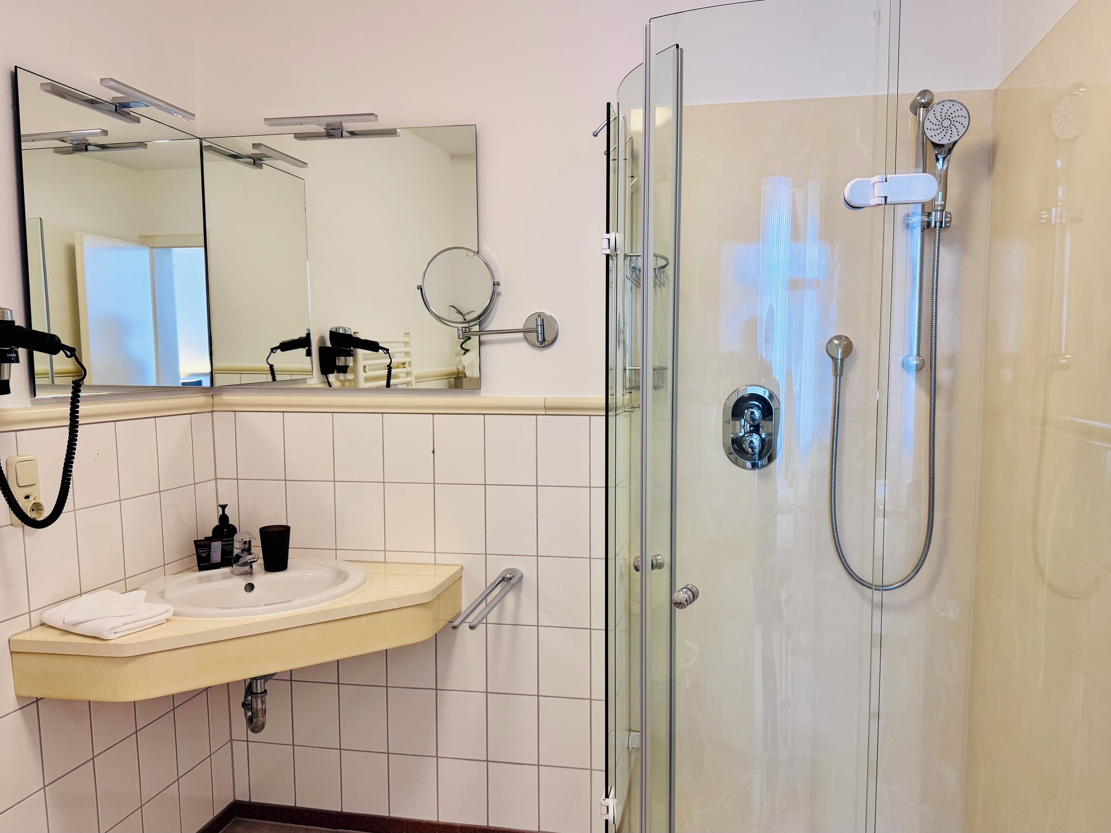 Une salle de bain moderne dotée d’une douche à parois de verre, d’un lavabo avec un meuble-vasque et d’un miroir surmonté d’un autre miroir rond.