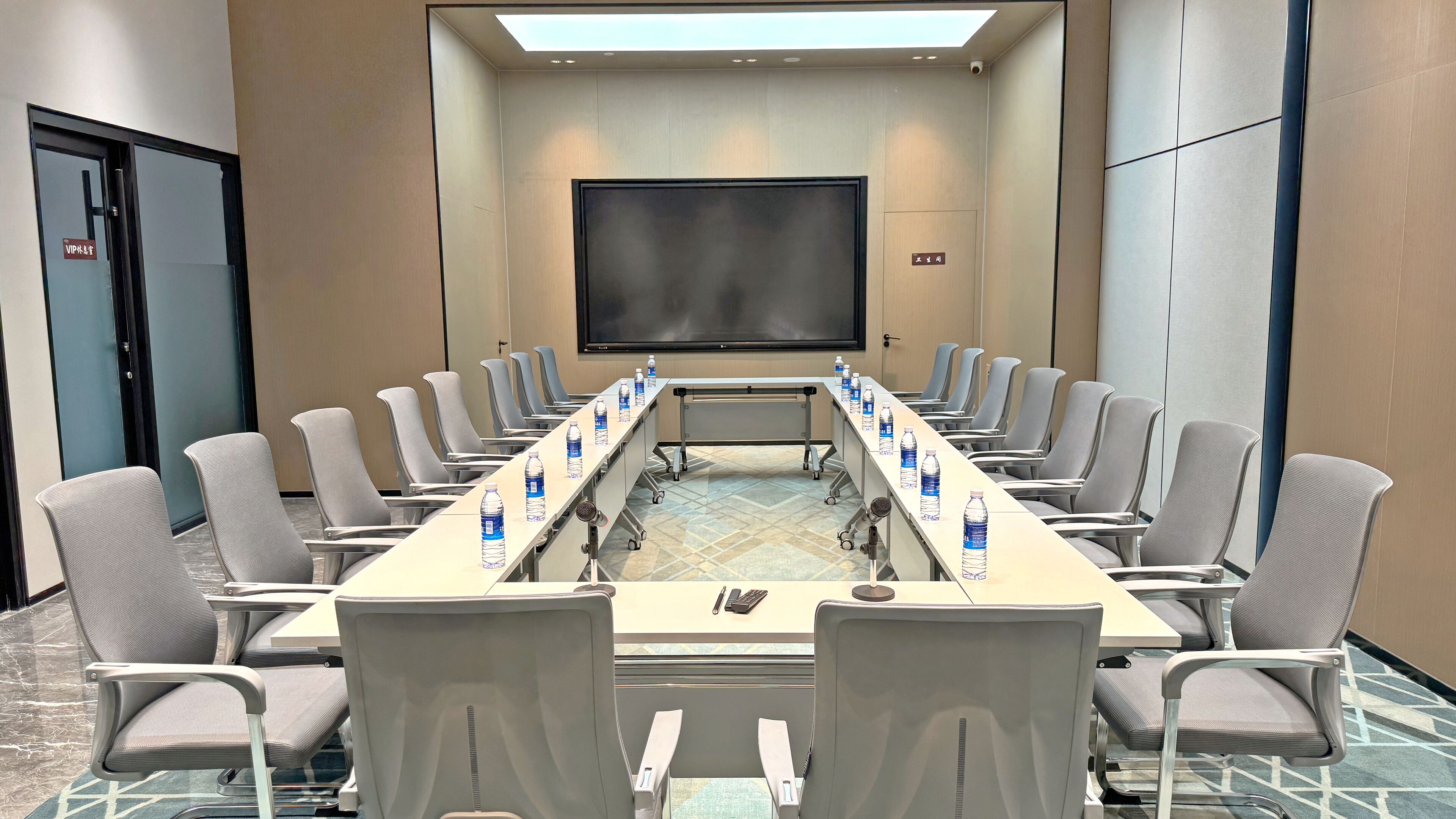 A conference room with a long table, chairs, water bottles, a projector screen, and a door with a VIP sign.