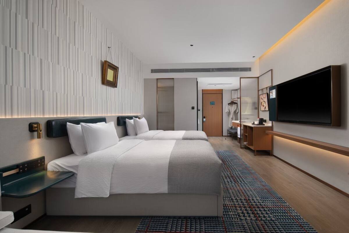 A modern hotel room with two beds, a large flat-screen TV, a desk, and a wardrobe.