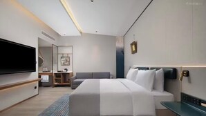 Ein modernes Hotelzimmer mit einem großen Bett, Nachttischen, einem Flachbildfernseher, einer Sitzecke und einer kleinen Küchenzeile.