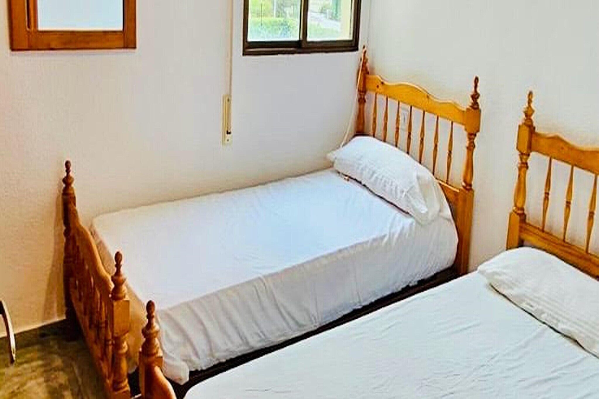 A small, single-bed room with wooden headboards and white bedding.