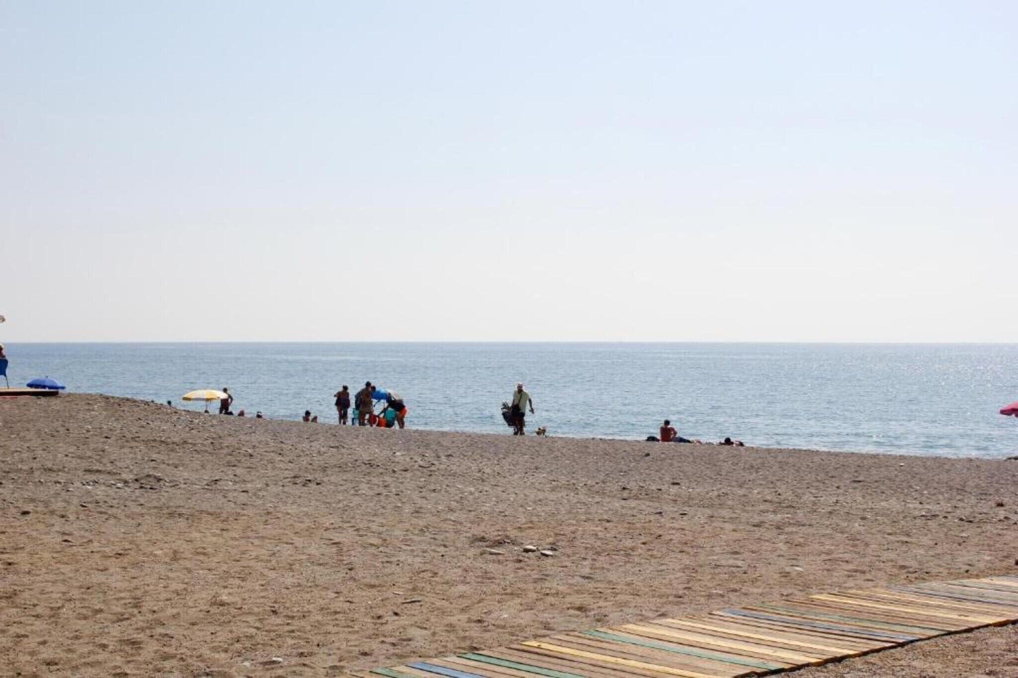 A beach with people, umbrellas, and a wooden boardwalk.