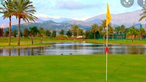 A golf course with a flagstick, water hazards, palm trees, and mountains in the background. - Apartment in Salobreña with Sea Views (Salobreña)