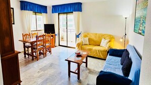 A living room with a yellow sofa, a blue couch, a wooden dining table with chairs, and a TV. - Apartment in Salobreña with Sea Views (Salobreña)