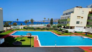 A swimming pool with a clear view of the sea, surrounded by greenery and a building with balconies. - Apartment in Salobreña with Sea Views (Salobreña)