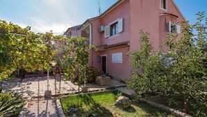 A pink house with a stone pathway leading to the entrance, surrounded by greenery and a clear sky. - Apartment Šibenik near Beach Gaj (Šibenik-Brodarica)